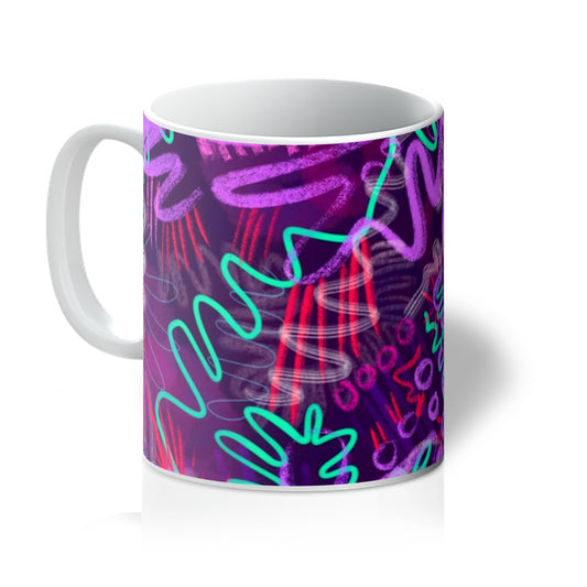 A white mug printed with art. The abstract design has aqua green squiggles, light and dark purple squiggles and circles and hot pink lines. Handle is on the left. 