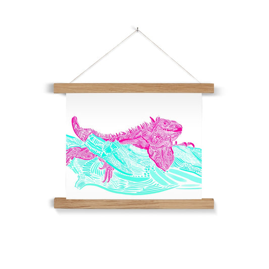 A light wooden poster hanger. The print background is white and the design is an Iguana laying on top of a branch. They are both rendered in lines, squiggles and circles. The Iguana is hot pink and the branch is seafoam green.