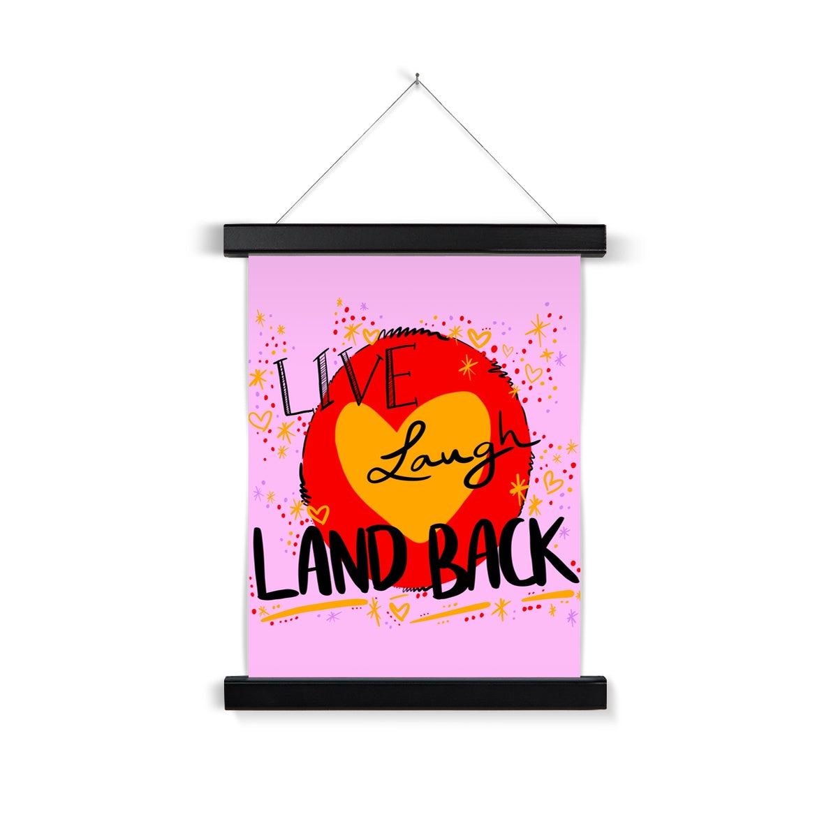 Black wooden poster hanger. The art print is rectangle. The design: ‘live laugh land back’ written in black with a yellow heart and red circle behind. The background is pink with small dots, squiggles, stars and hearts dotted around the image in red, yellow and purple.