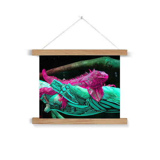  A light wooden poster hanger. A digital collage: a photo of an Iguana laying on a branch, doodles are rendered on the Iguana and the branch. The iguana is pink and the branch is seafoam green.
