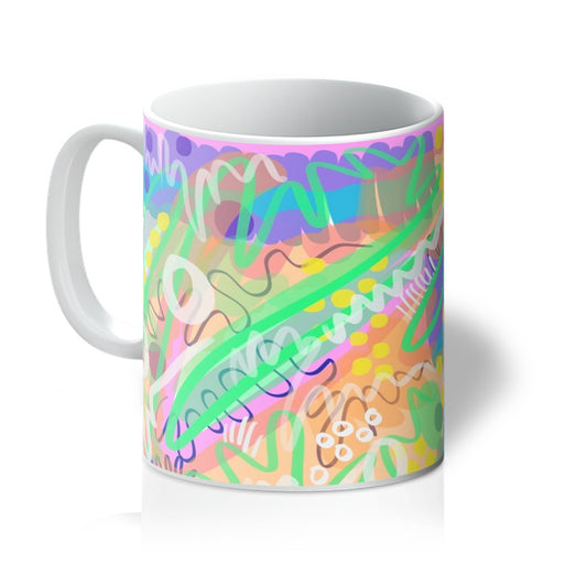 White mug with art print. Abstract line drawing. It uses green/yellow/purple/pink/blue/yellow. The colours are fresh and bright. there are circles, squiggles and dots. Handle is on the left. 