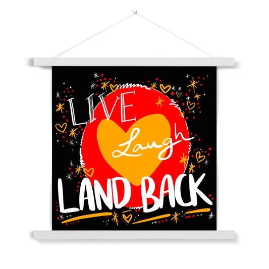 A white wooden poster hanger. The print is square. The design: ‘live laugh land back’ written in white with a yellow heart and red circle behind. The background is black with small dots, squiggles, stars and hearts dotted around the image in red, yellow and white.