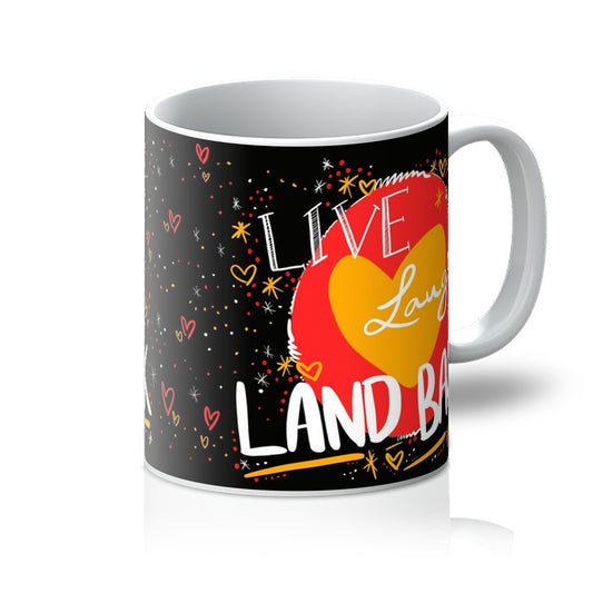 White mug with art print. ‘live laugh land back’ written in white with a yellow heart and red circle behind. The background is black with small dots, squiggles, stars and hearts dotted around the image in red, yellow and white. Handle is on the right. 